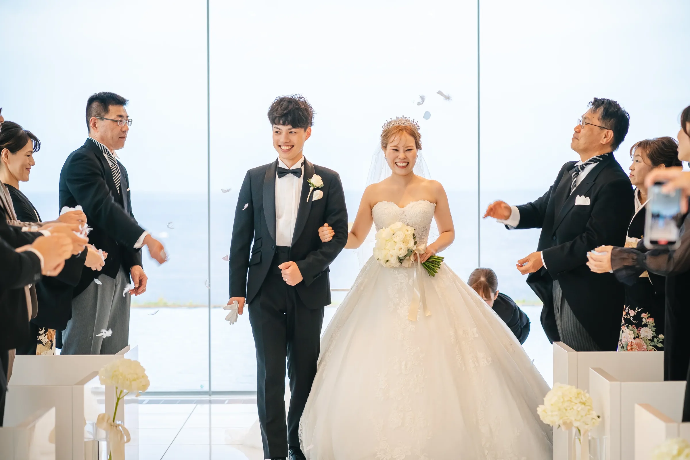 チャペルで花びらのシャワーを受けながら歩く新郎新婦と白いブーケ
