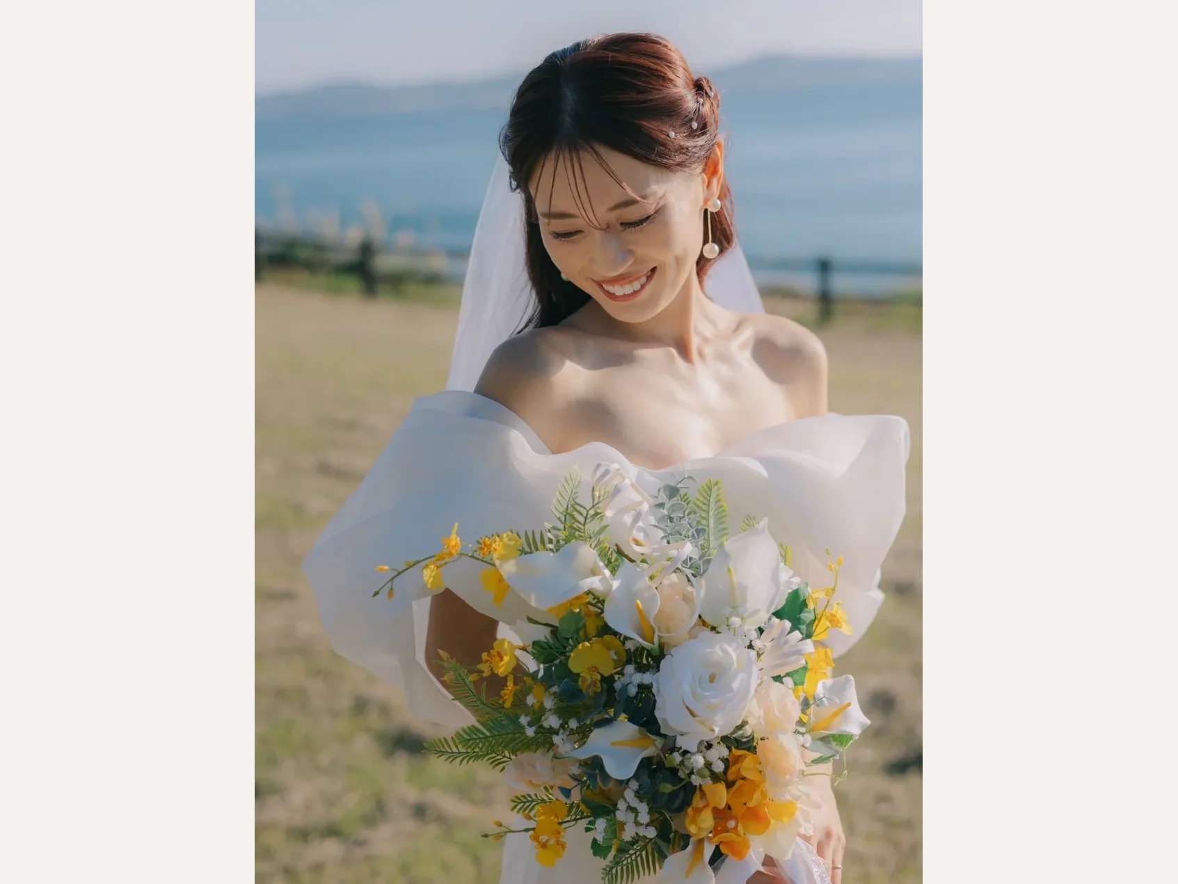 海辺の草地で白と黄色のブーケを持つ白いドレスの花嫁