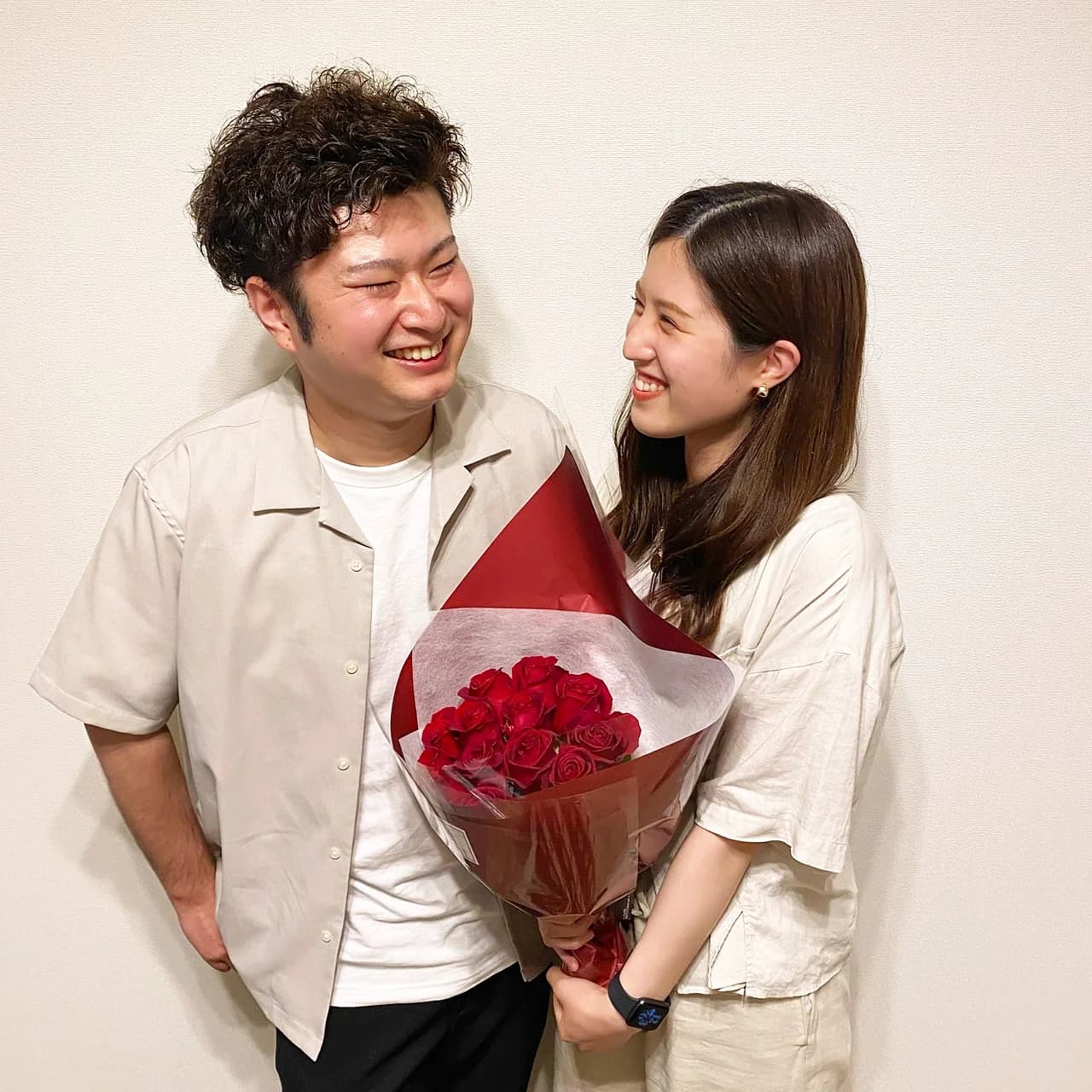 白い壁の前で赤いバラの花束を持って笑い合うカップル